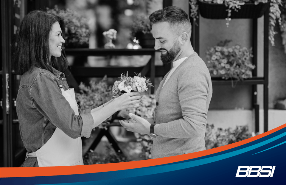 Owner of a small floral shop hands a man a brightly colored bouquet of flowers