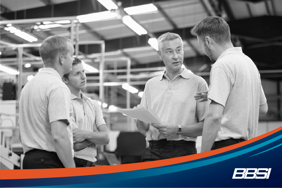 A group of men standing in a factory discussing corrective action planning.