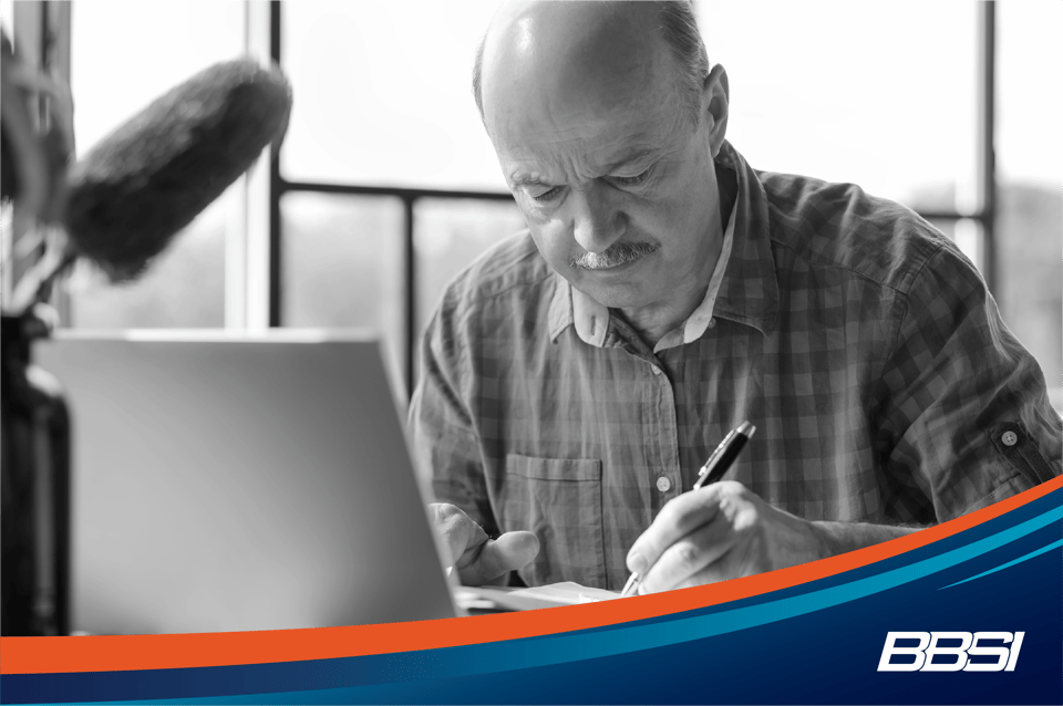 Man sitting a desk writing down notes in front of a laptop