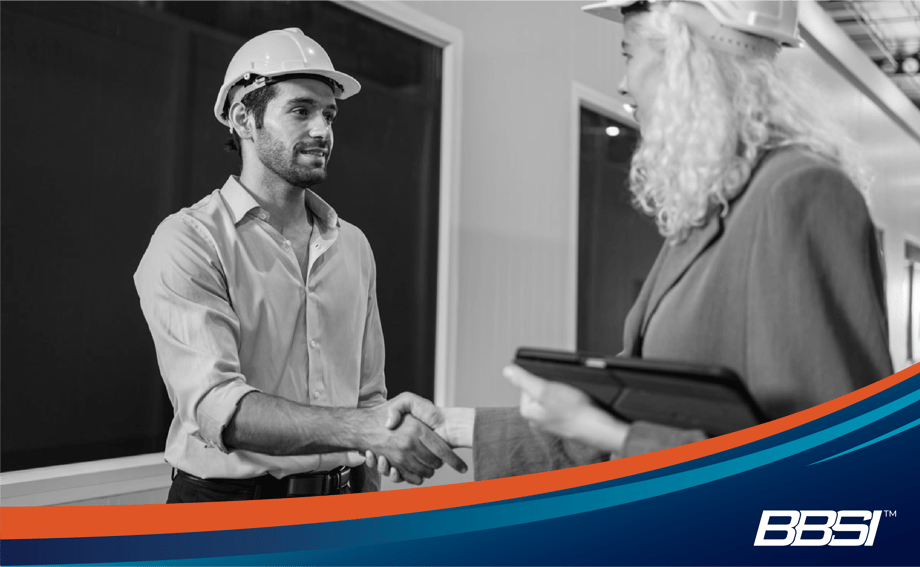 Workers shake hands in hard hats during a workers compensation compliance safety check.