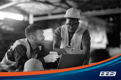 Two colleagues drinking coffee while working on a laptop at a wood warehouse.