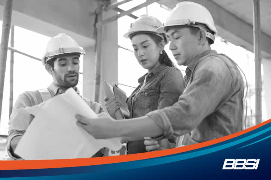 three employees on a job site looking at plans right after attending a safety meeting