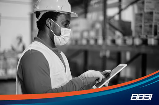 Worker wearing safety protective gear using an iPad in a warehouse.