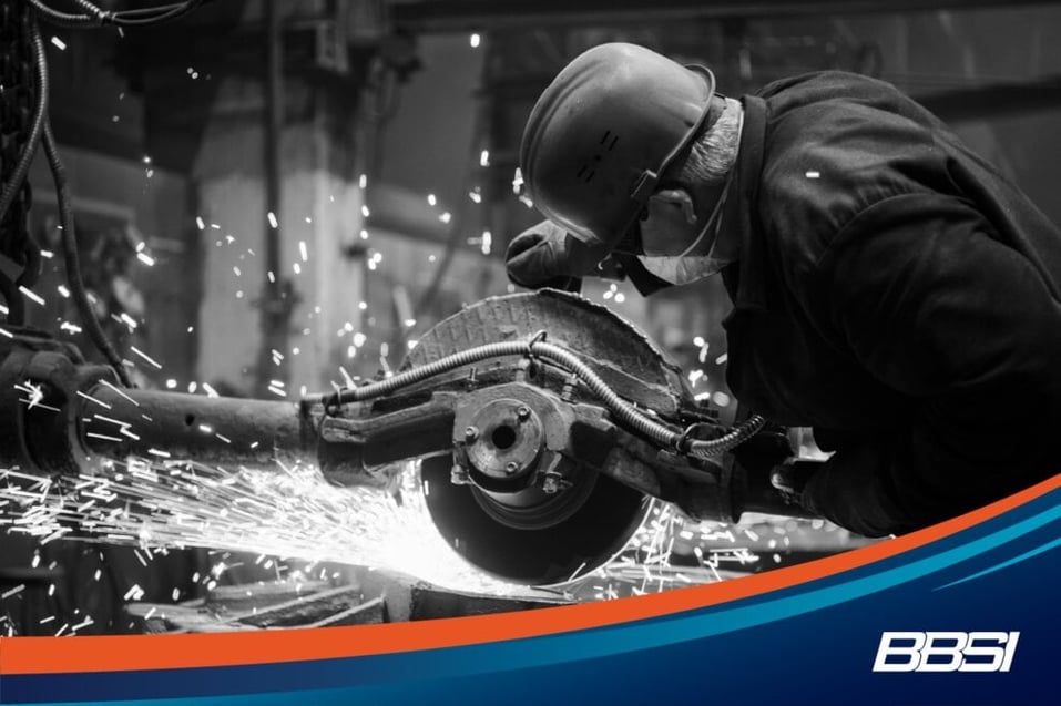 Worker wearing a red hard hat grinding and cutting metal.