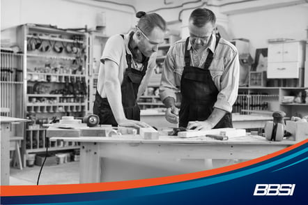 Older carpenter training a younger employee in a workshop