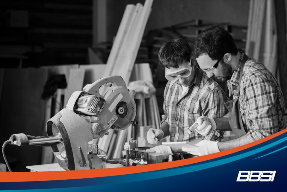 Two carpenters training in a carpentry workshop using a machine and working off notes