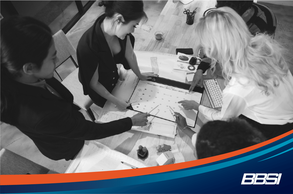 Group of colleagues standing around a table looking at a calendar.