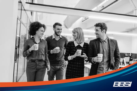 Four coworkers walking together in an office chatting over coffee.