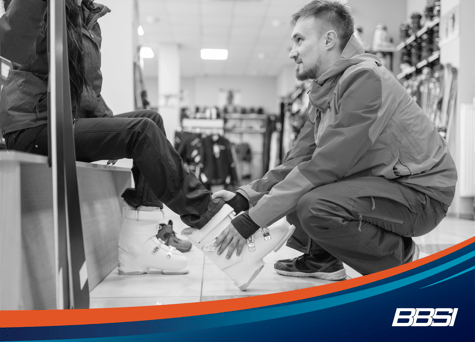 man is helping woman try on a snowshoe at his seasonal snowboard shop