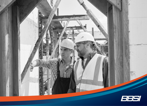 two men wearing hard hats are investigating a piece of wood on a construction site 