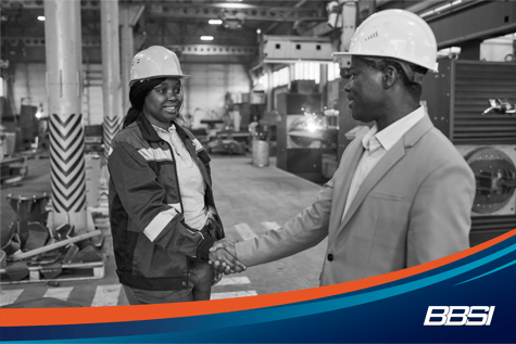  A man and woman shake hands on a job site wearing hard hats