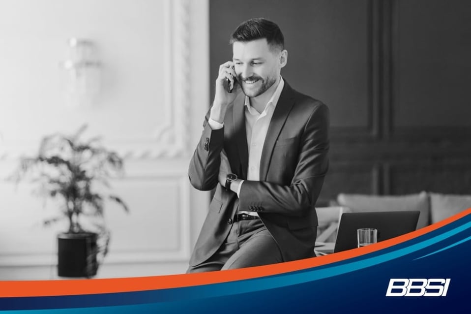 Businessman wearing a navy blue suit talking on his phone while sitting on his table.