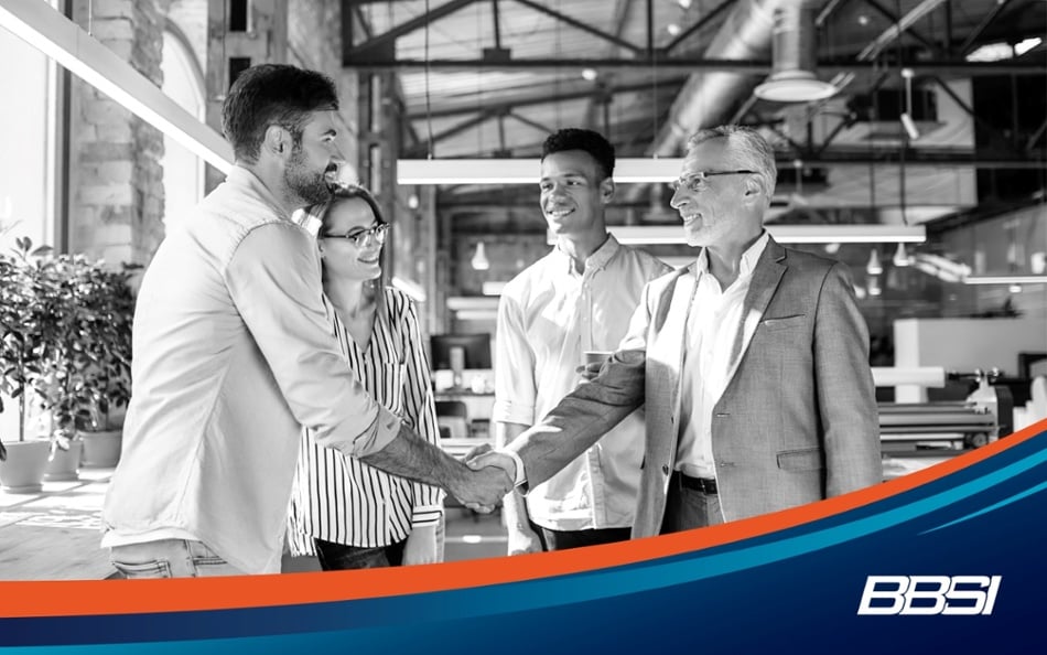 One man is shaking hands with a businessman wearing a suit in an office next to two colleagues.