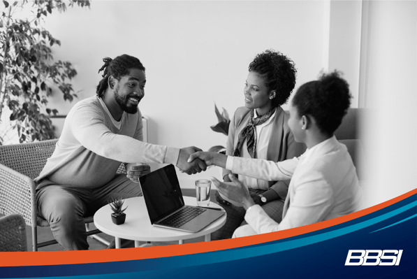 Man shaking hands with 2 people sitting down at a meeting