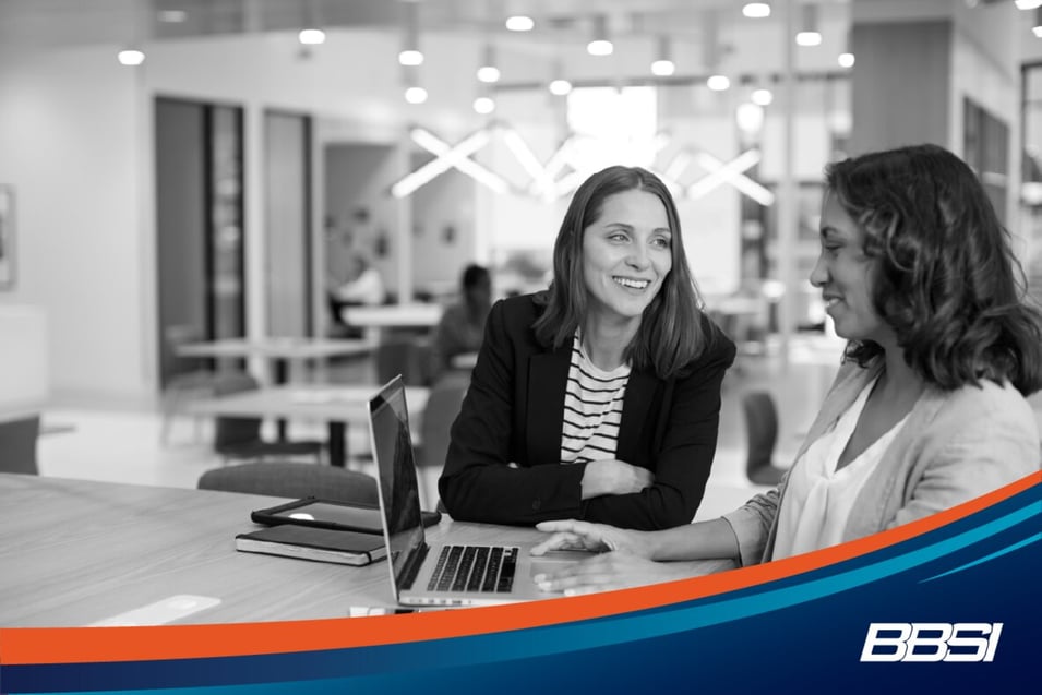 woman advising another woman while she works on her laptop in an office