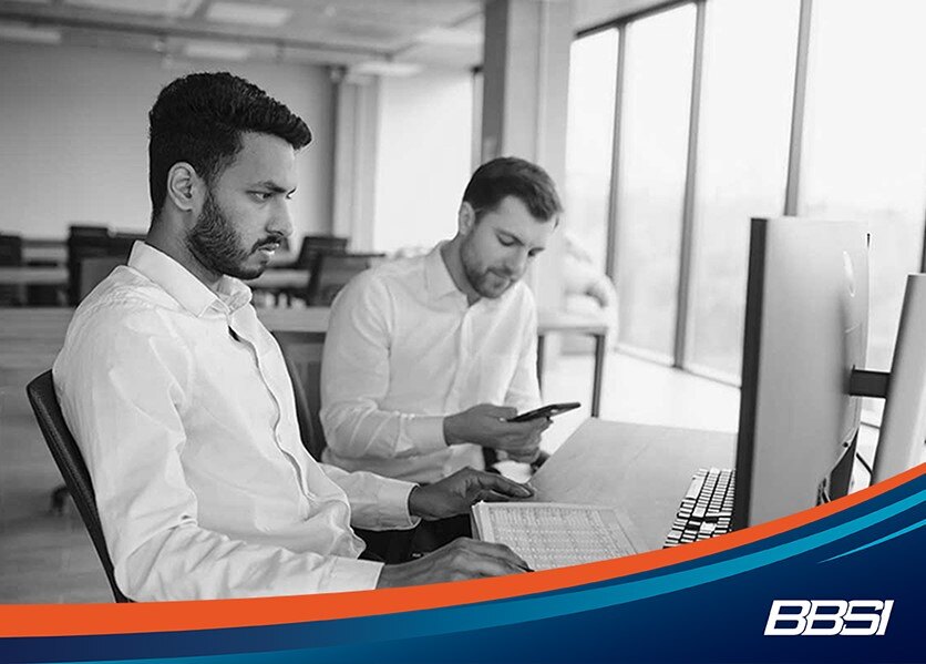 two businessmen sitting at a computer discussing open enrollment 2024