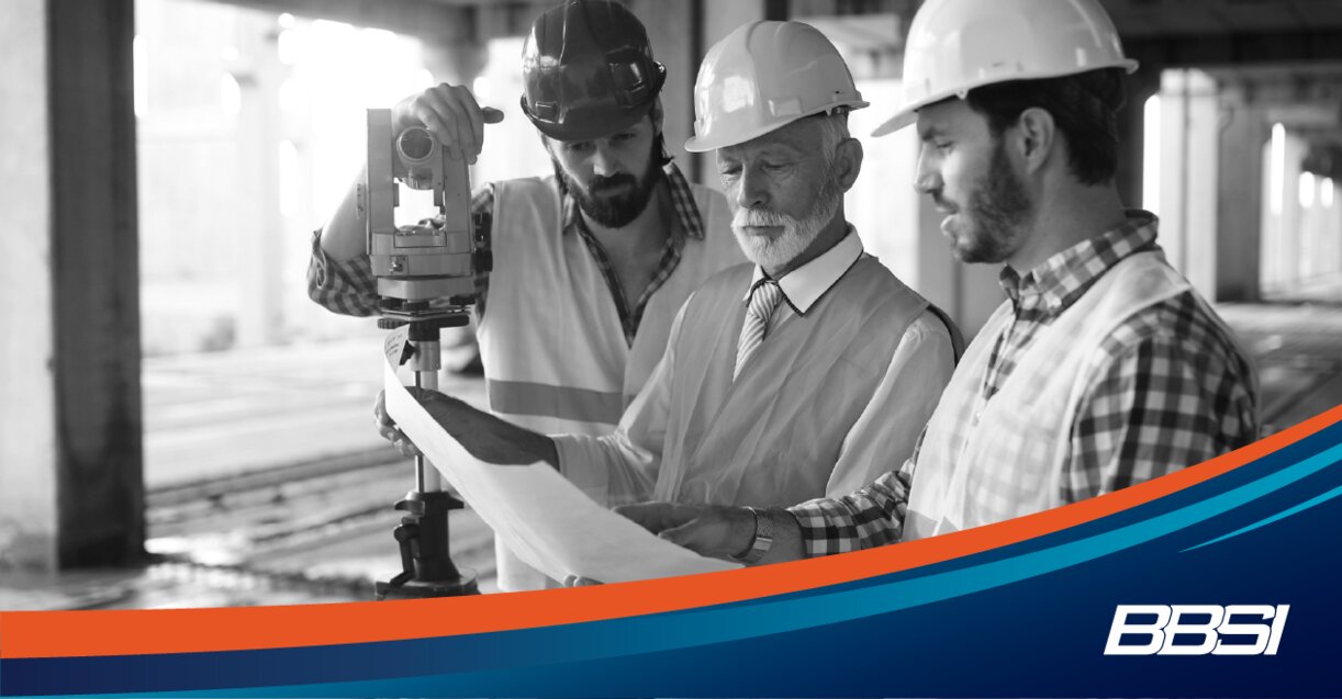 Construction workers wearing neon safety vests and hard hats looking over a blueprint.