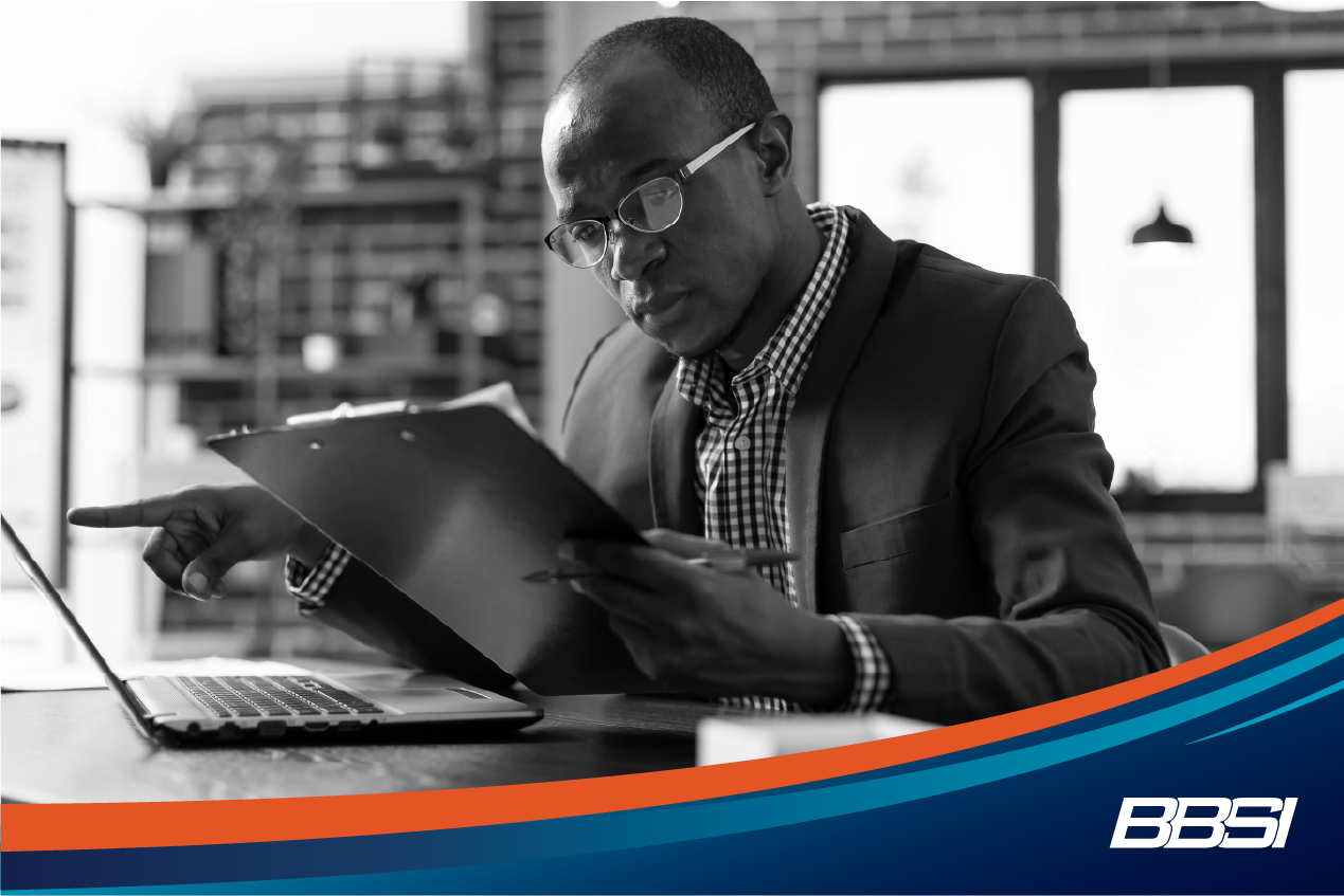 A man sitting at a desk, reading from a clipboard, going over employee benefits.