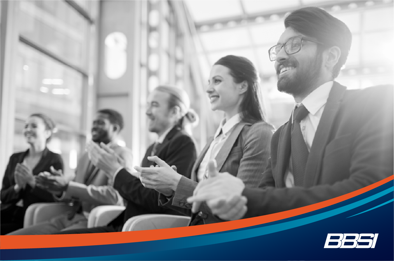 Group of business men and women clapping at an event.