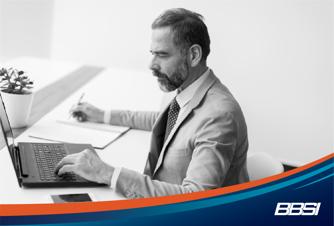 Man working at a desk on his laptop and taking notes.