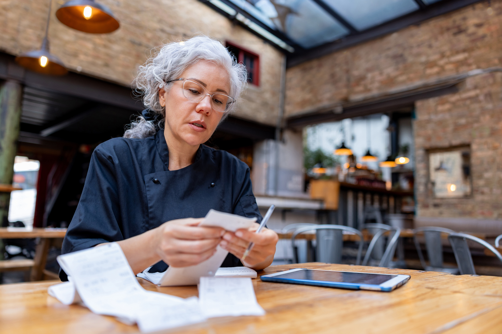 Restaurant owner reviewing receipts with a tablet nearby for reporting.